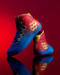 RUDIS Wonder Woman Hildebrandt 2.0 girls' wrestling shoes displayed against a red background, featuring red and blue uppers, gold logos and reflective styling.