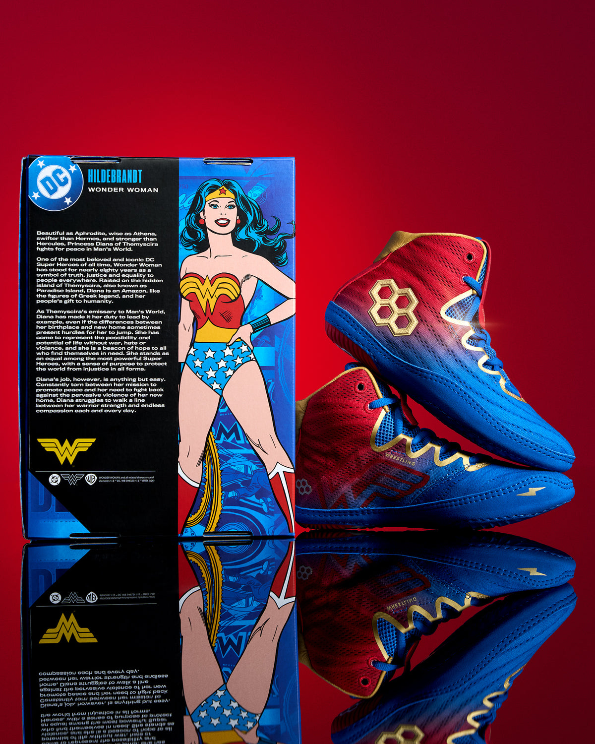 RUDIS Wonder Woman Hildebrandt 2.0 girls' wrestling shoes beside DC Wonder Woman collector packaging, featuring red, blue and gold superhero-inspired details.