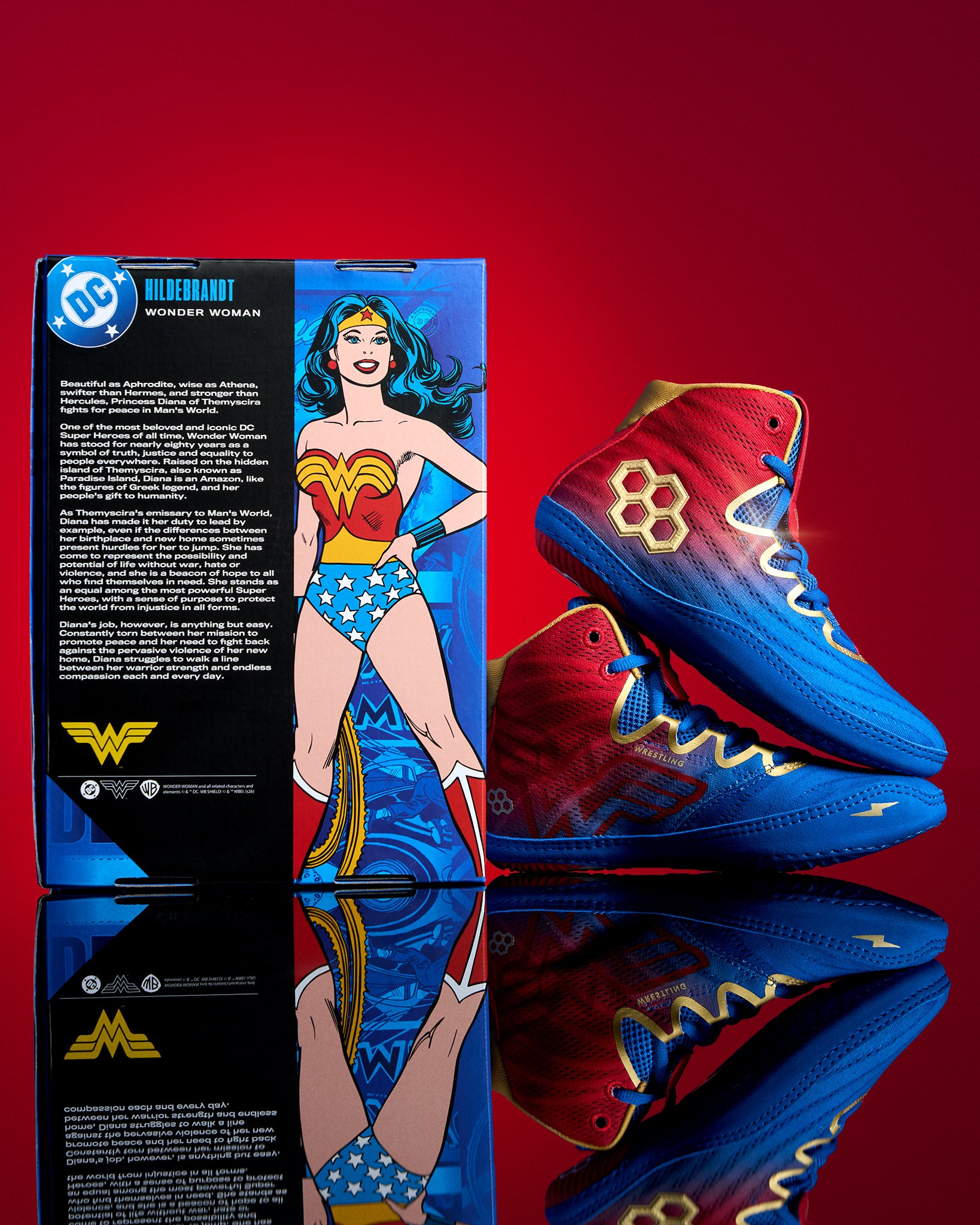 RUDIS Wonder Woman Hildebrandt 2.0 girls' wrestling shoes beside DC Wonder Woman collector packaging, featuring red, blue and gold superhero-inspired details.