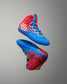 RUDIS Wonder Woman Hildebrandt 2.0 girls' wrestling shoes shown in an elevated display, highlighting blue and red uppers, gold RUDIS logos and Wonder Woman graphics.