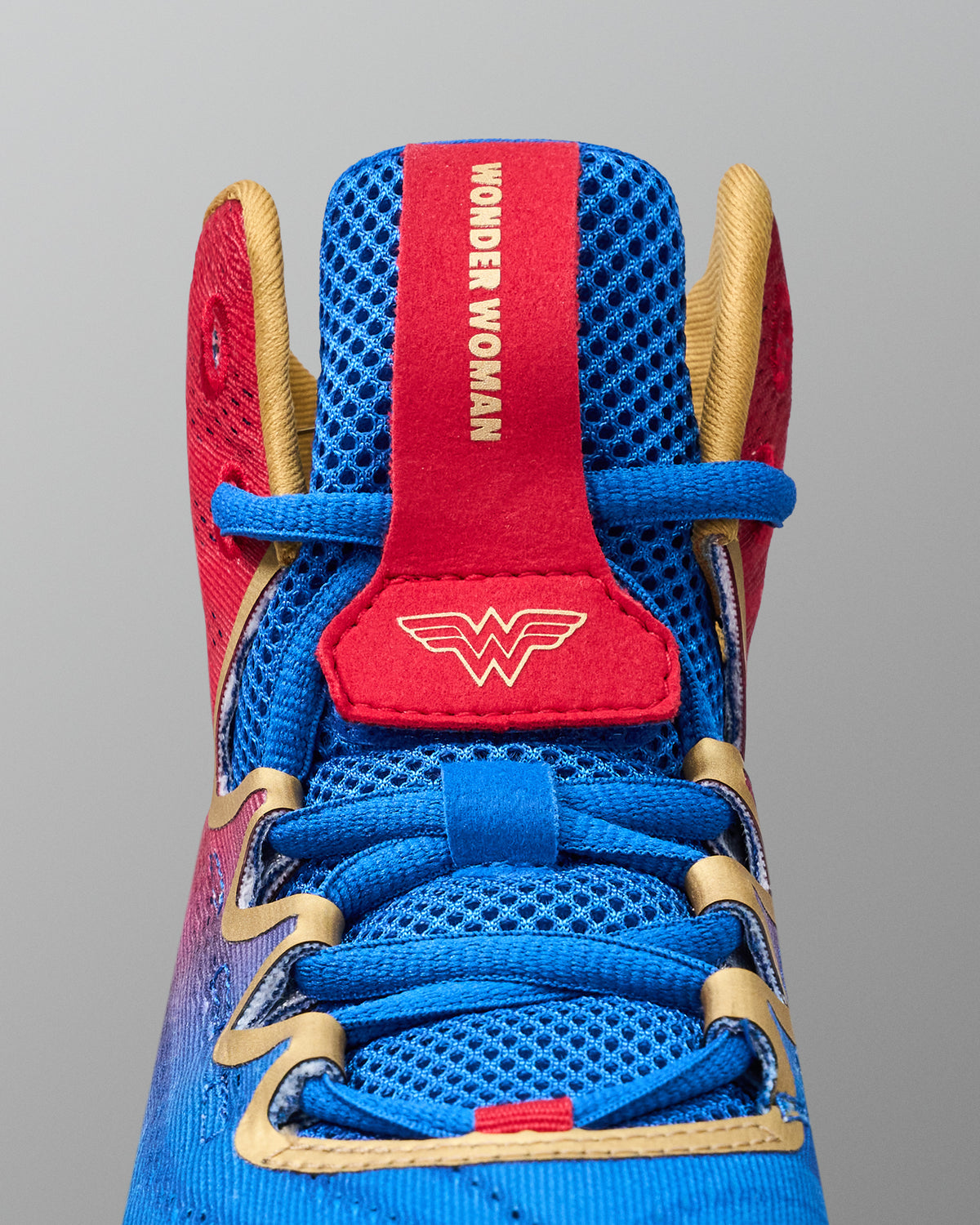 Close-up of RUDIS Wonder Woman Hildebrandt 2.0 girls' wrestling shoe showing blue mesh, blue laces, gold eyelet trim and red Wonder Woman logo tongue.