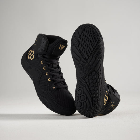 Black high-top wrestling shoes with gold accents on a light gray background